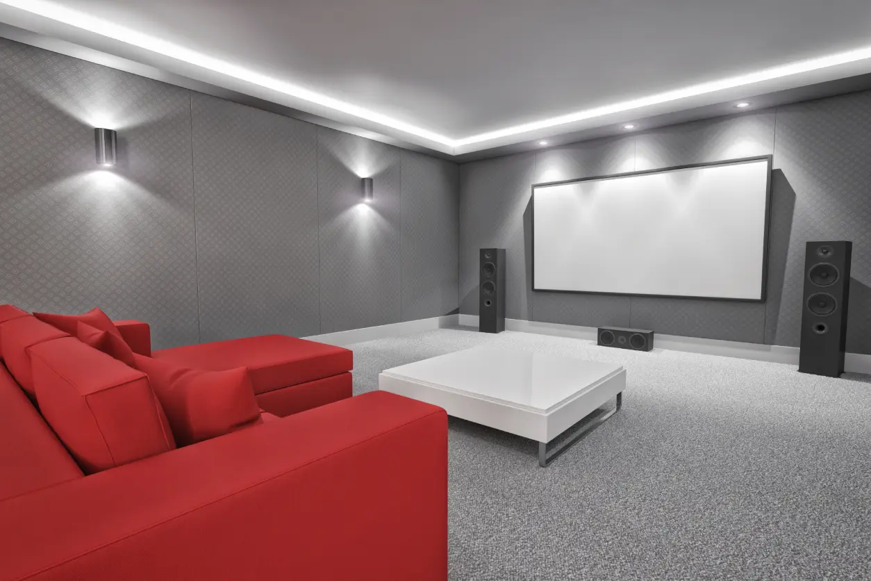 Home theater with red sofa, white coffee table, large screen, and speakers in a gray walled room with ceiling lights.